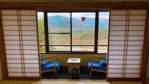 A traditional Japanese room with tatami flooring, a futon bed, and a view of autumn foliage through a shoji screen. - Kurobe Sun Valley Hotel (Omachi)