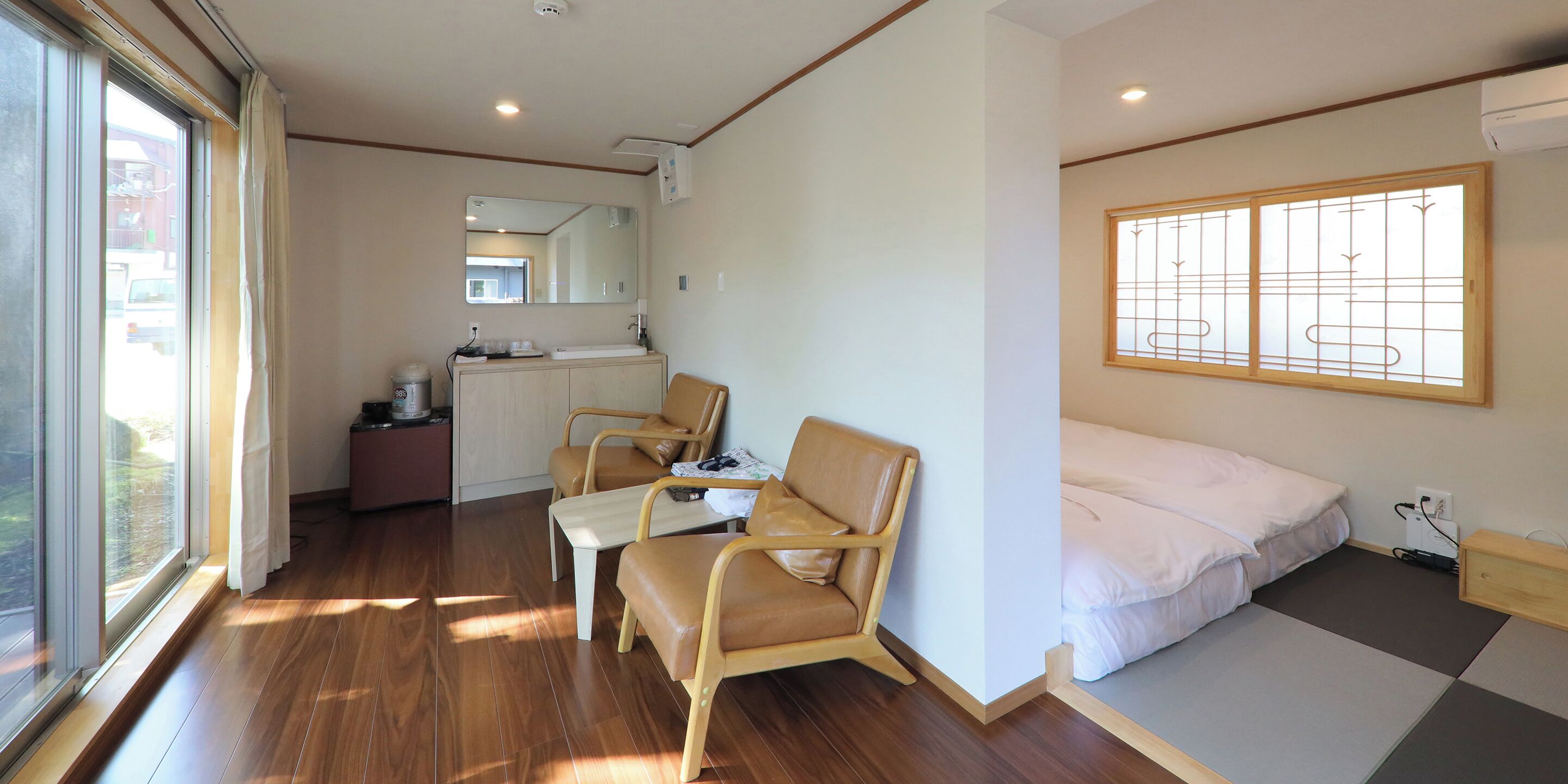A room with a bed, a desk, two chairs, a window, and a mirror.