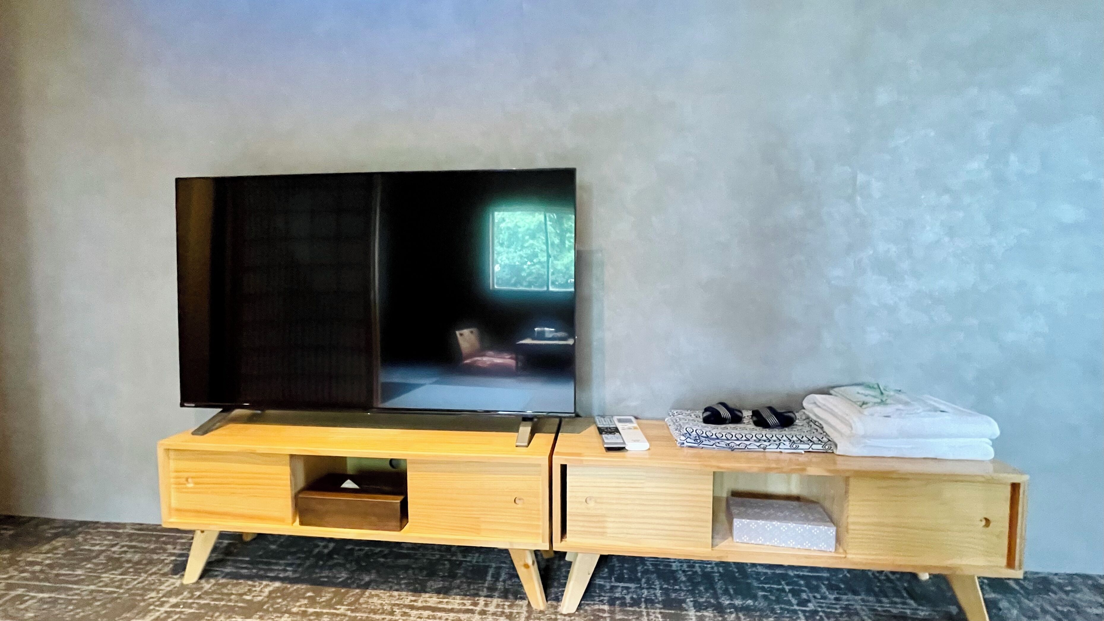Un meuble en bois pour la télévision, avec un téléviseur à écran plat, une télécommande et une paire de chaussons.