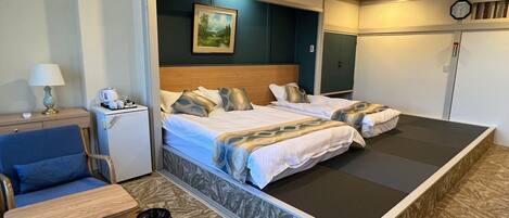 Ein Hotelzimmer mit zwei Betten, einem Schreibtisch, einem Stuhl, einem kleinen Tisch und einer Wanduhr.