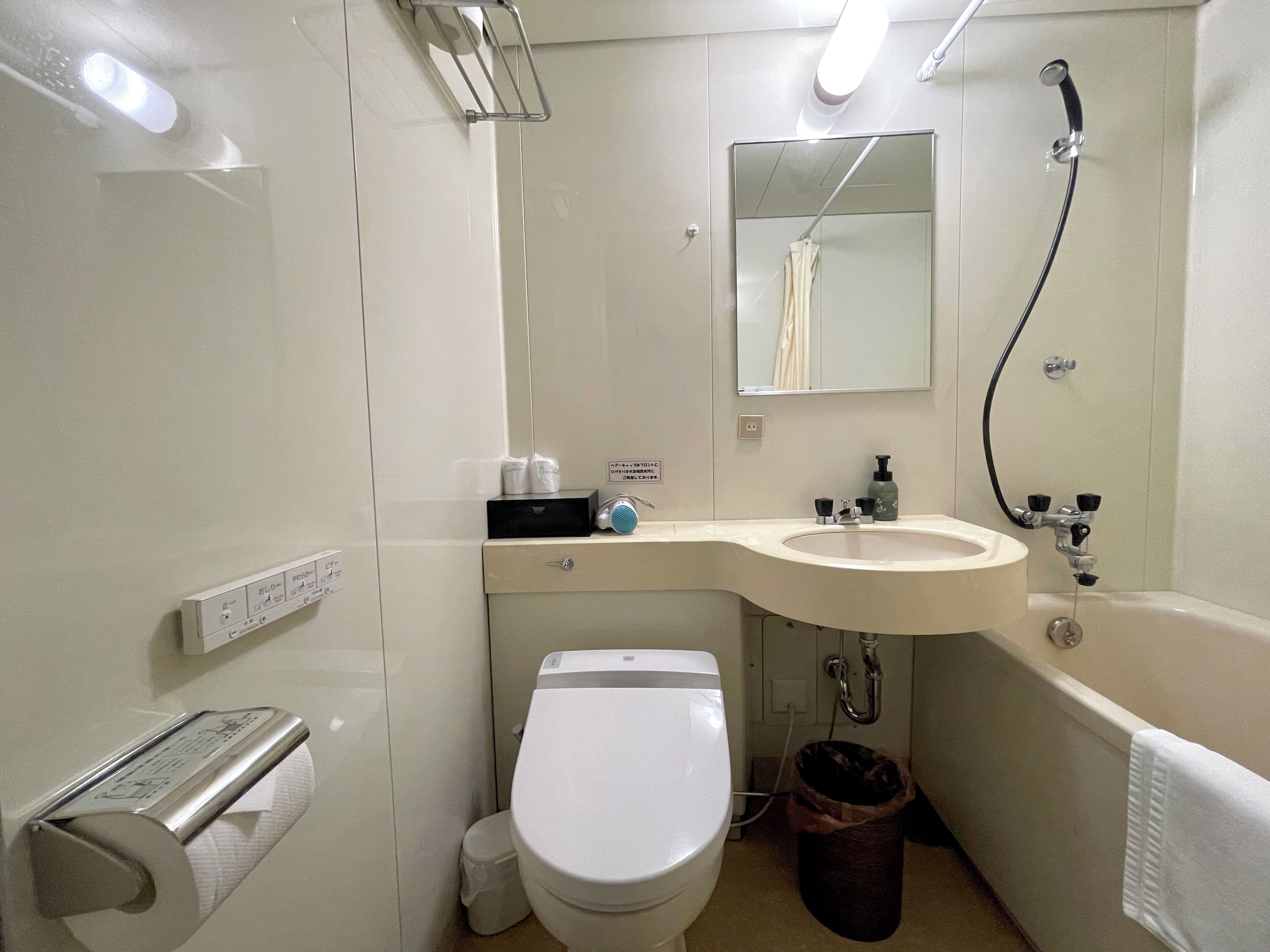 A bathroom with a toilet, sink, and shower. There are towels and toiletries on the counter.