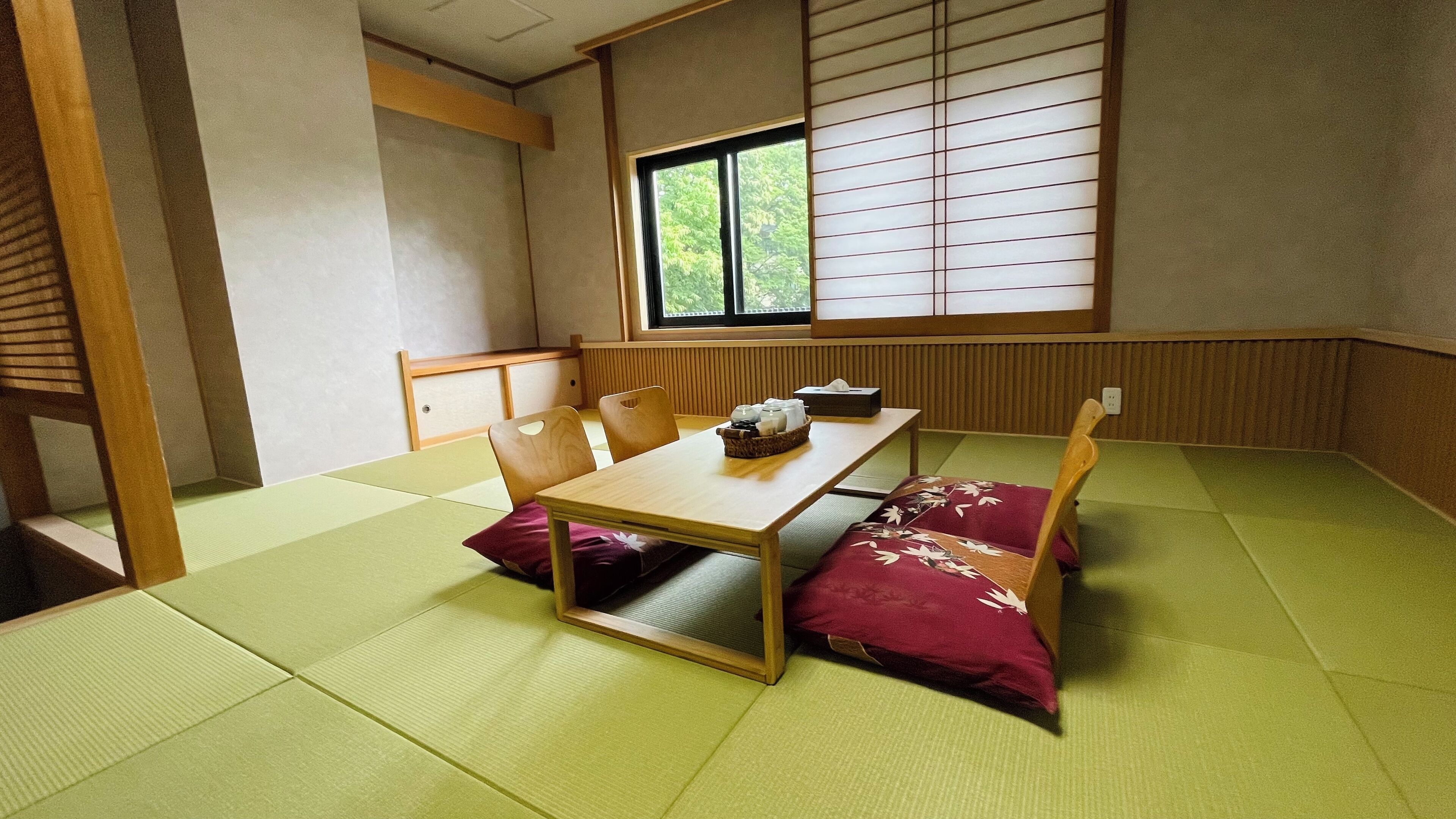 A tatami mat room with a low table, chairs, and a window with shoji screens.