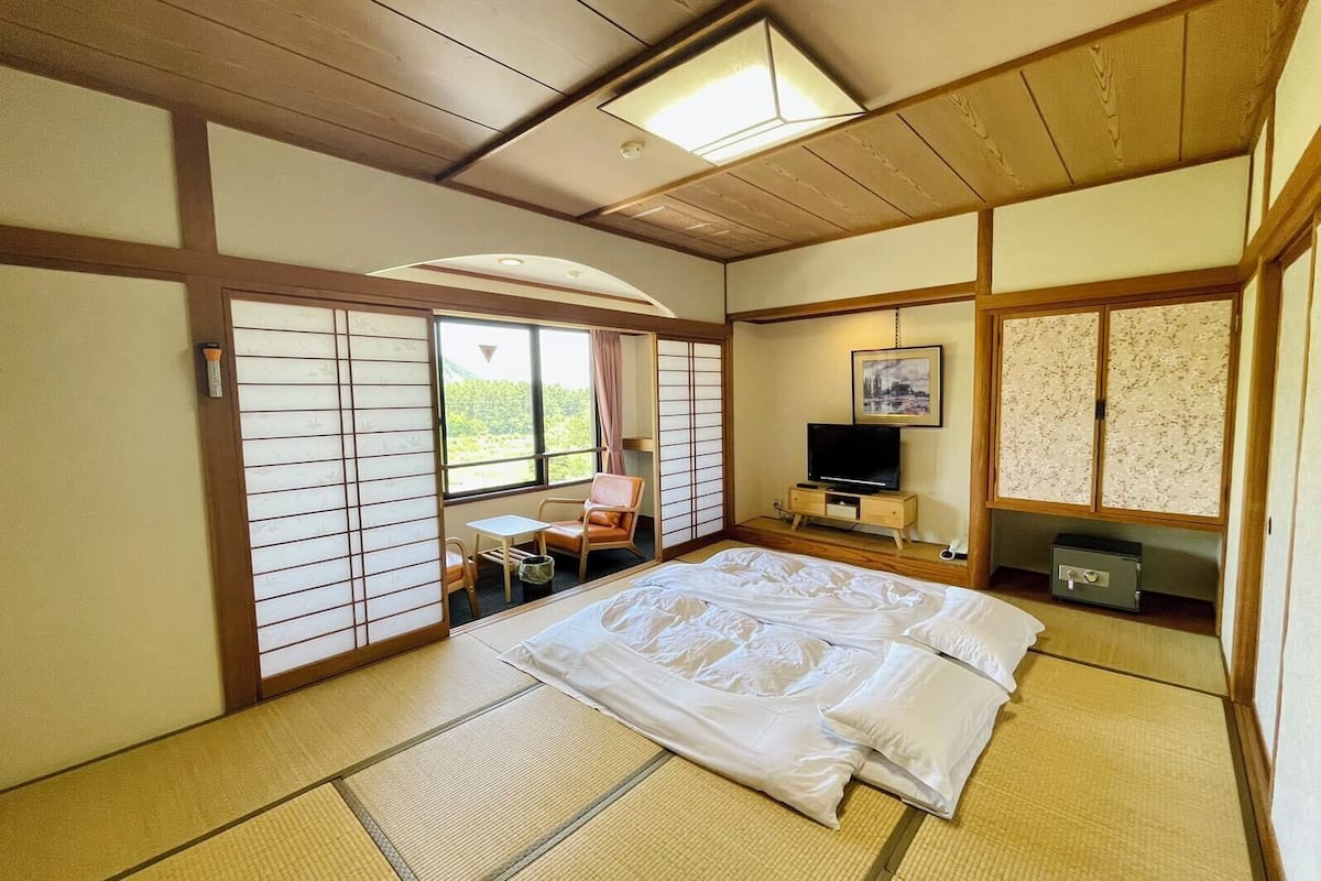 A traditional Japanese-style room with tatami flooring, a bed, a television, and a sliding door.