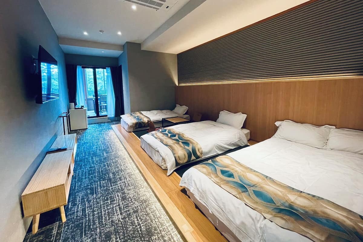 A hotel room with two beds, a desk, and a large window.