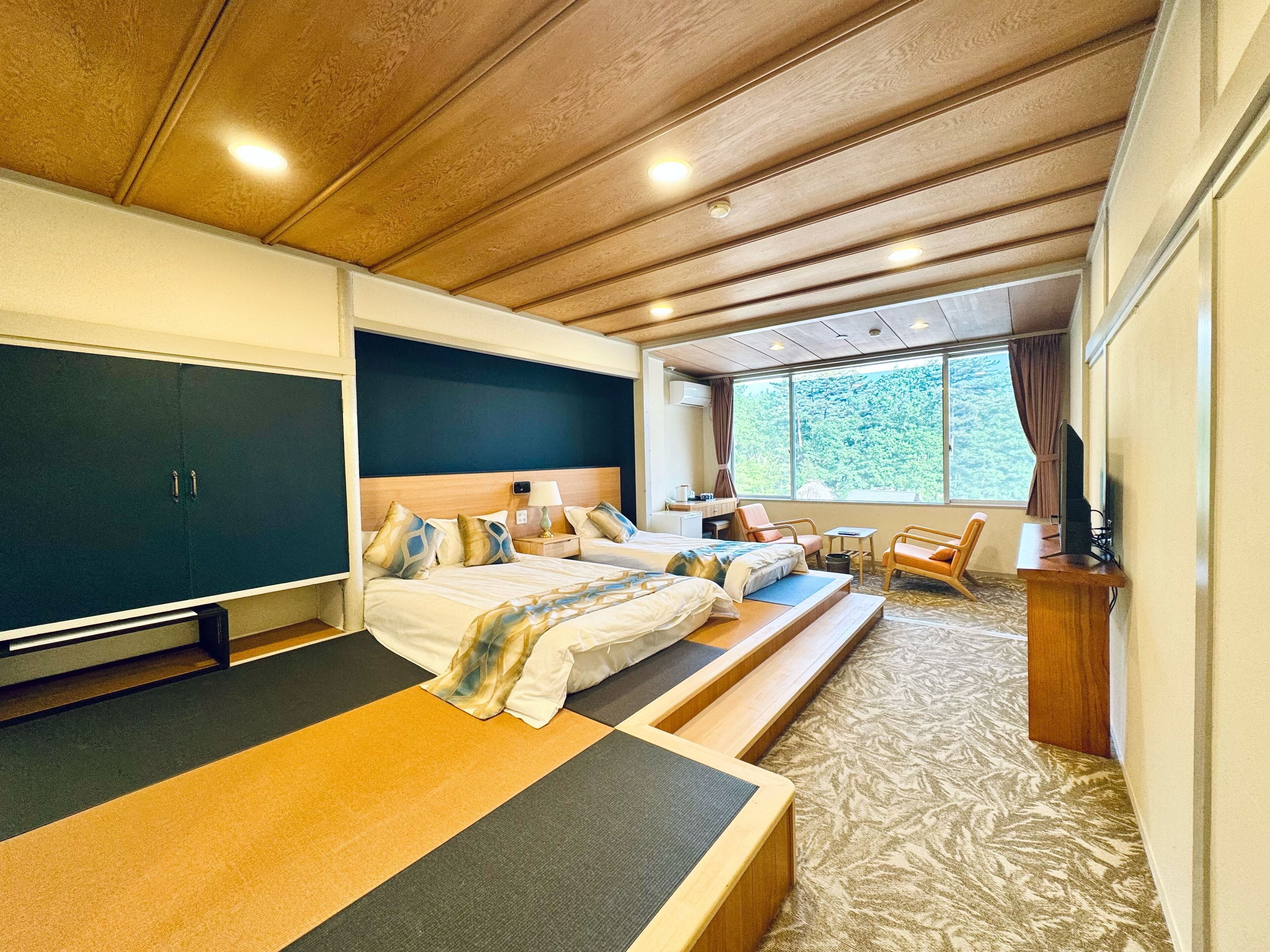 A spacious bedroom with a large bed, a desk, and a window with a view of trees.