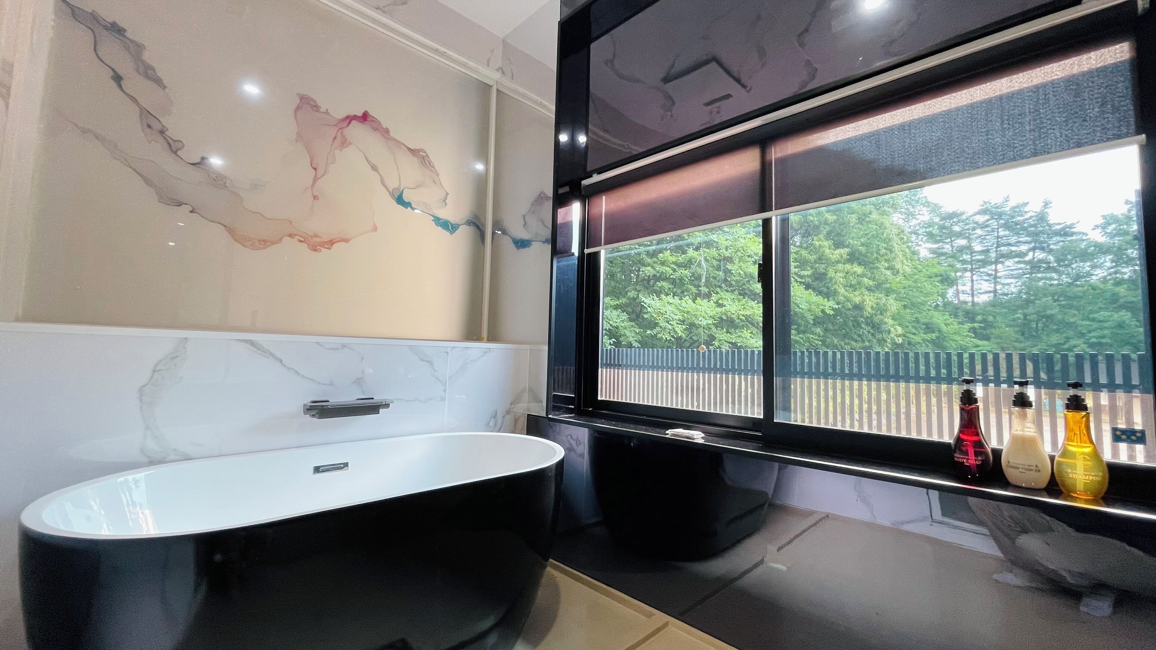 Une salle de bain moderne avec une baignoire sur pieds, un mur en marbre et une fenêtre donnant sur une terrasse en bois et un espace verdoyant.