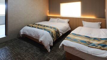 A hotel room with two beds, a patterned bedspread, a wooden headboard, and a window with blinds.