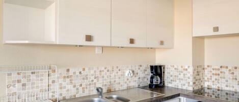 A modern kitchen with white cabinets, a tiled backsplash, a coffee maker, and a microwave.