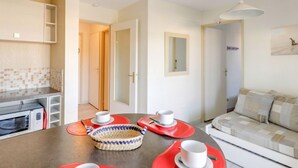 Una cucina moderna con forno a microonde, un tavolo da pranzo con tovagliette rosse e un cesto di vimini. Si vede anche un divano e un quadro appeso al muro.