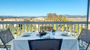 Un balcone con un tavolo apparecchiato per due persone, vista su una città con montagne sullo sfondo.