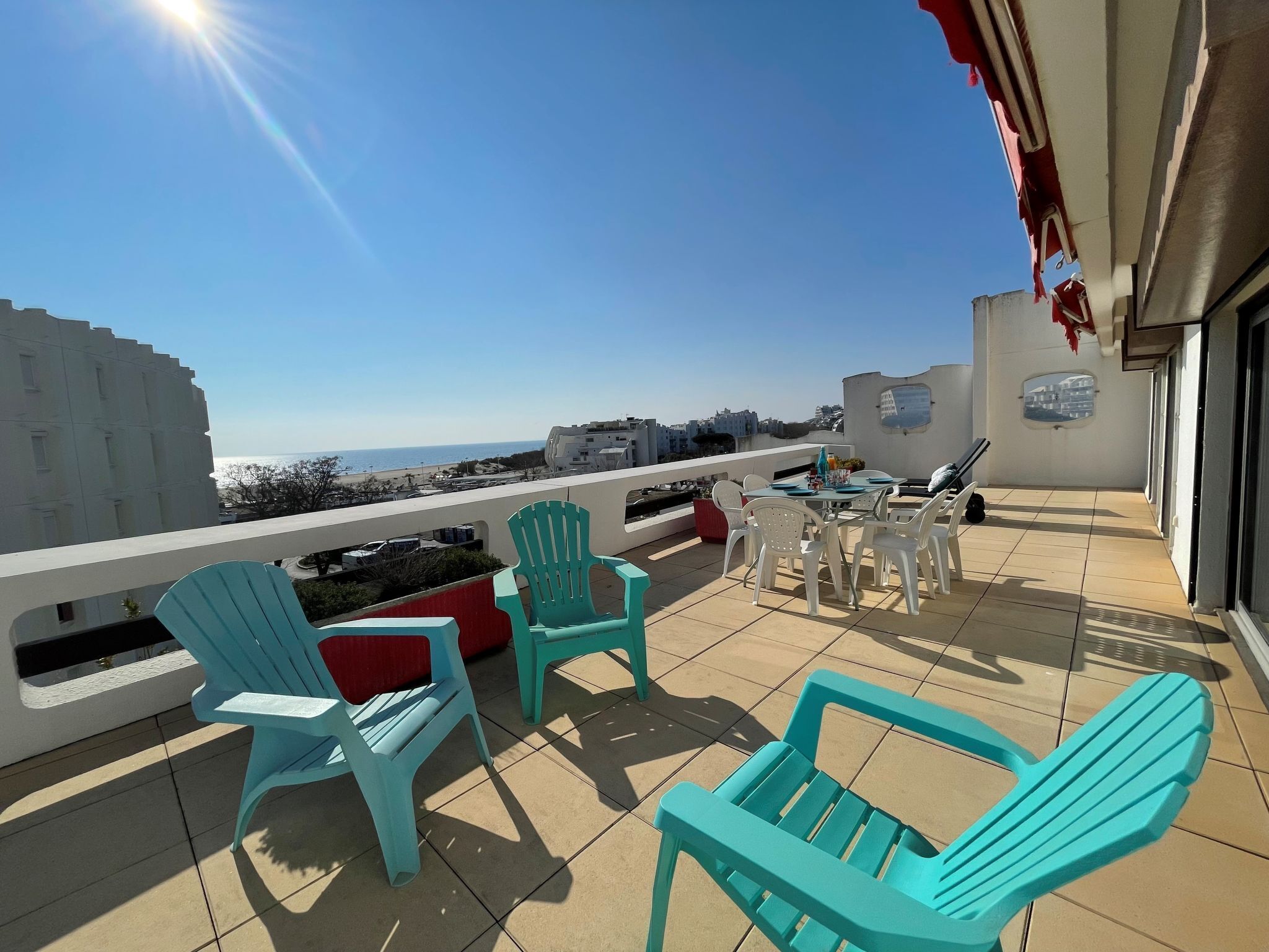 A balcony with turquoise chairs, a table, and a view of the sea.