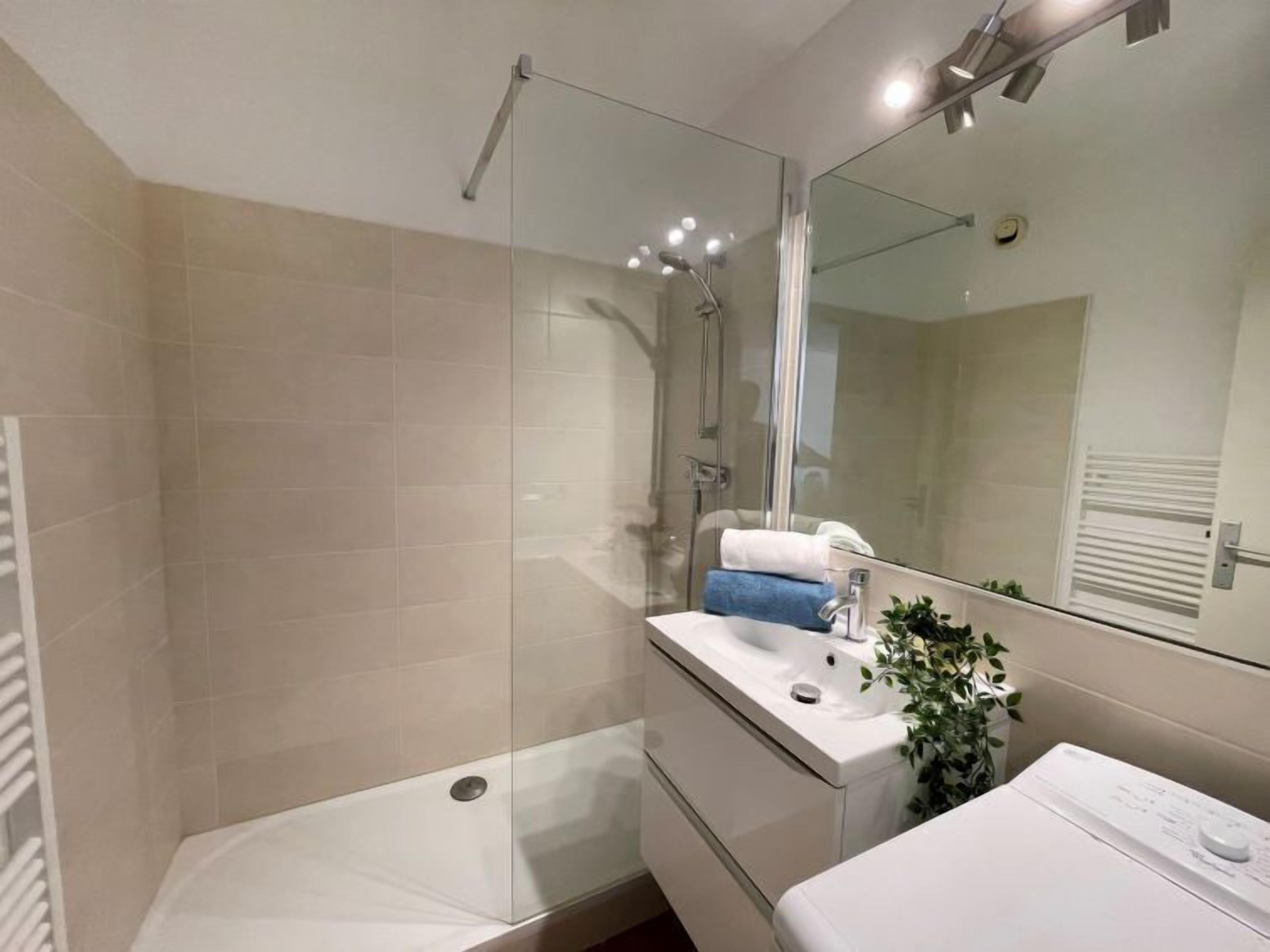 Une salle de bain moderne avec une douche à l’italienne en verre, un lavabo blanc et un grand miroir.
