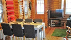 A wooden cabin interior with a dining table, four chairs, a television, and a fireplace. - Vacation home Rihka by Interhome (Hämeenlinna)