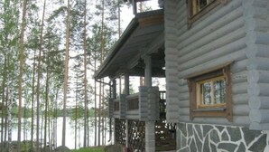 A log cabin with a stone foundation, a porch, and a view of a forest and water. - Vacation home Rihka by Interhome (Hämeenlinna)