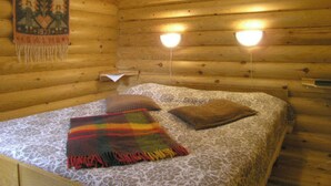 A wooden cabin room with a bed, a wall tapestry, and two wall-mounted lights. - Vacation home Rihka by Interhome (Hämeenlinna)