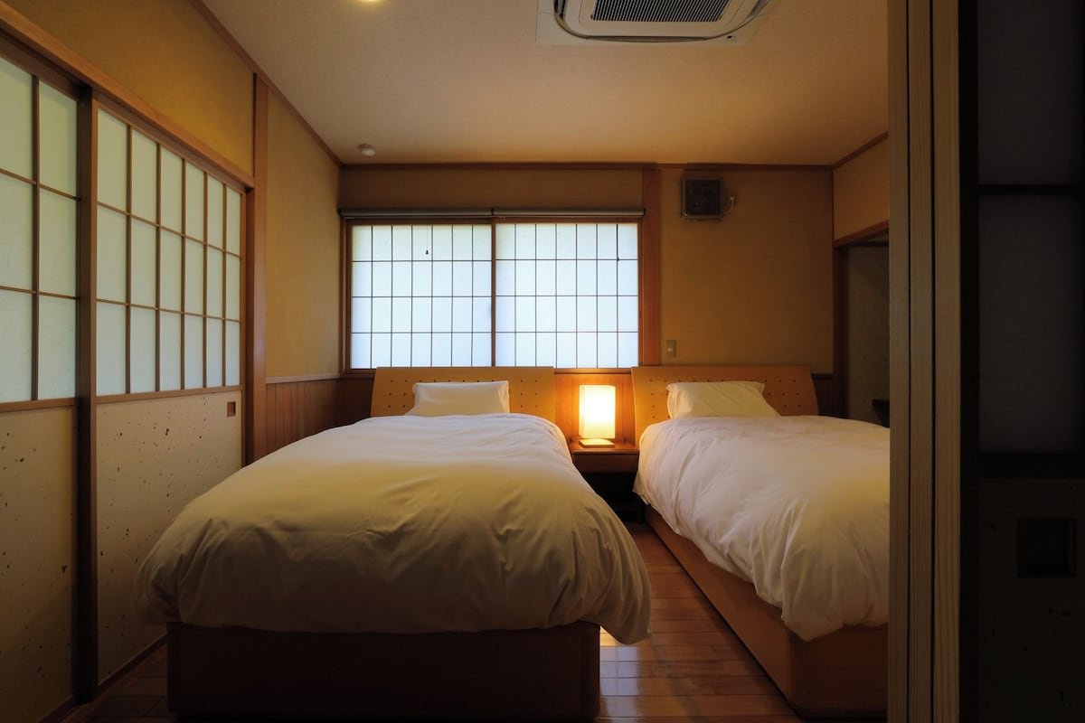 Habitación de hotel con dos camas, ventana con vistas y una lámpara de noche.