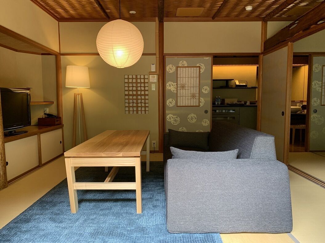 Habitació japonesa tradicional amb sòl de tatami, una taula de fusta baixa, un sofà, un fanal de paper penjant i portes corredisses.