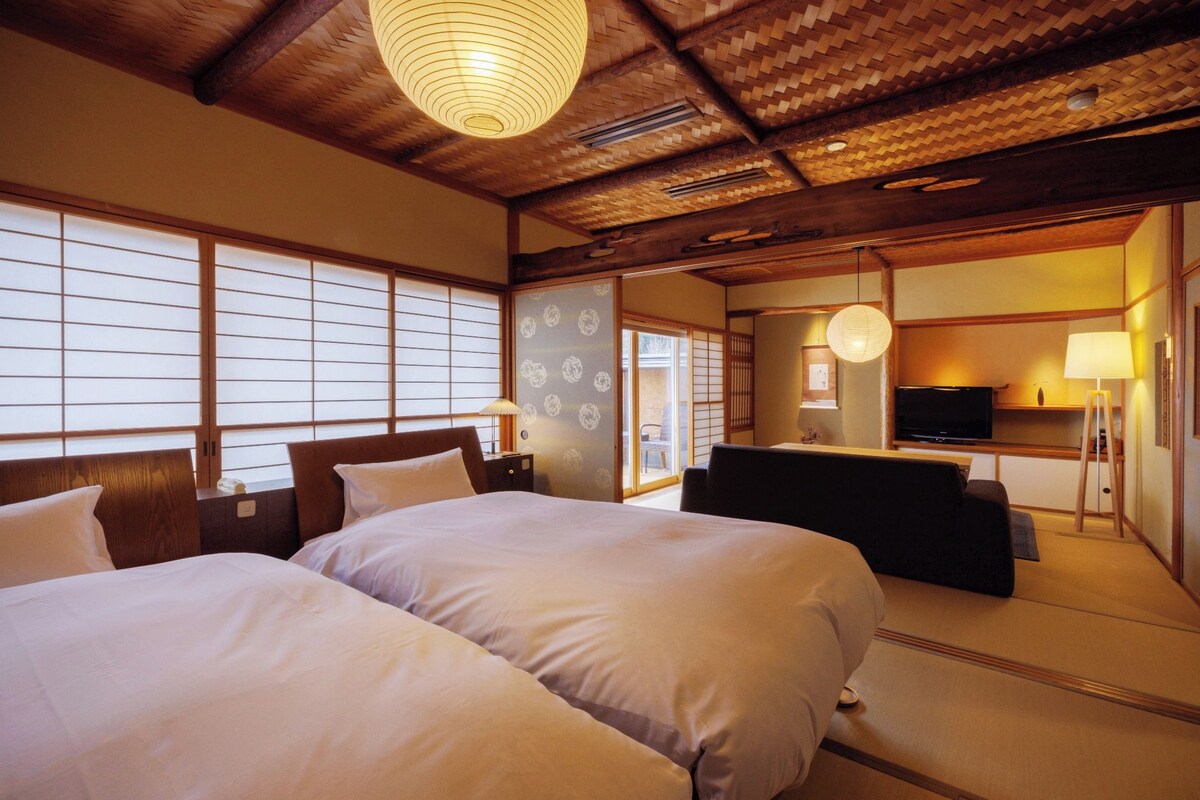 Habitación de hotel con dos camas, un sofá, un televisor y una puerta corredera tradicional japonesa.