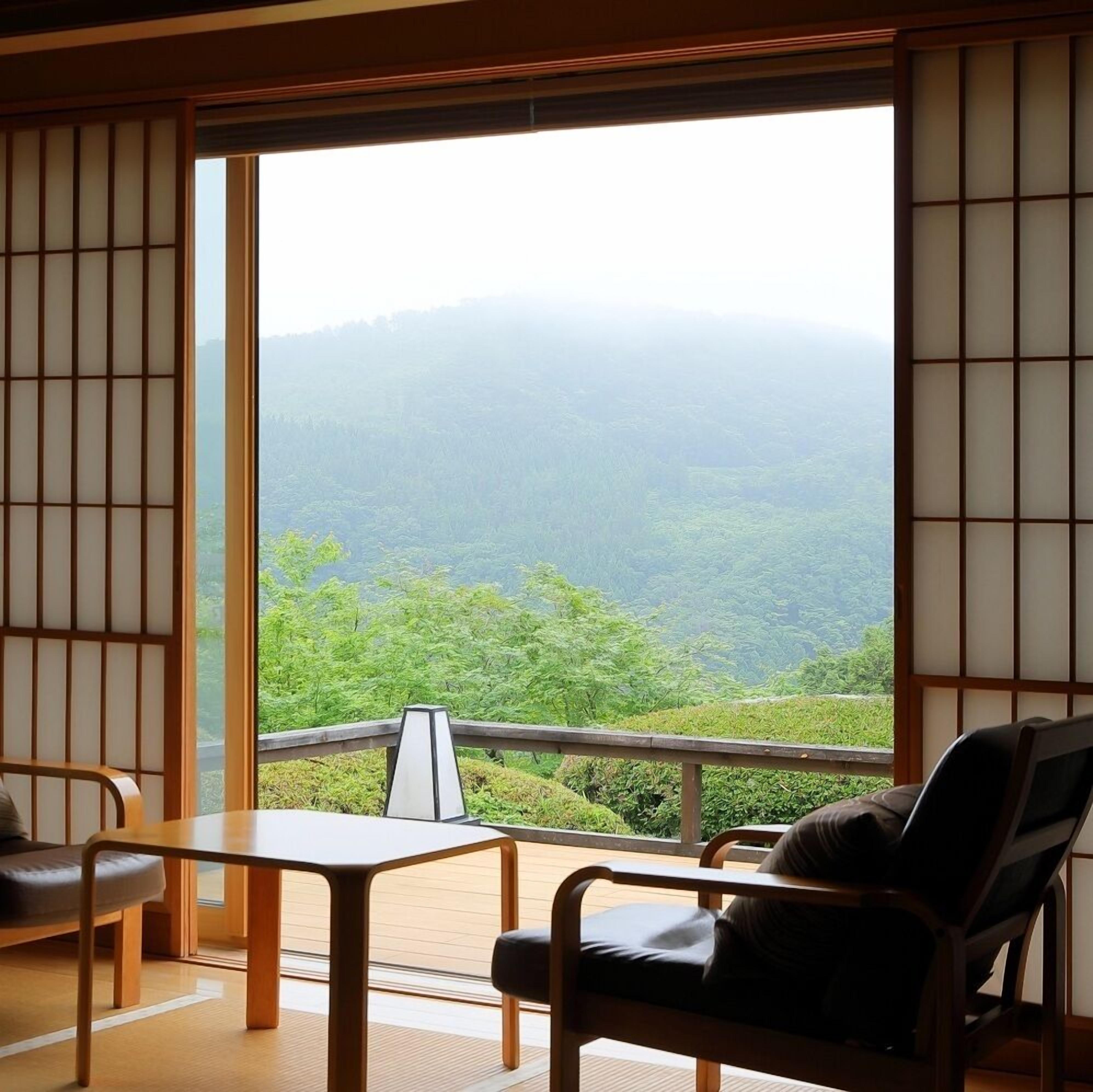 Habitació amb paviment de tatami, una taula baixa, una cadira i vista a una serralada boscosa.