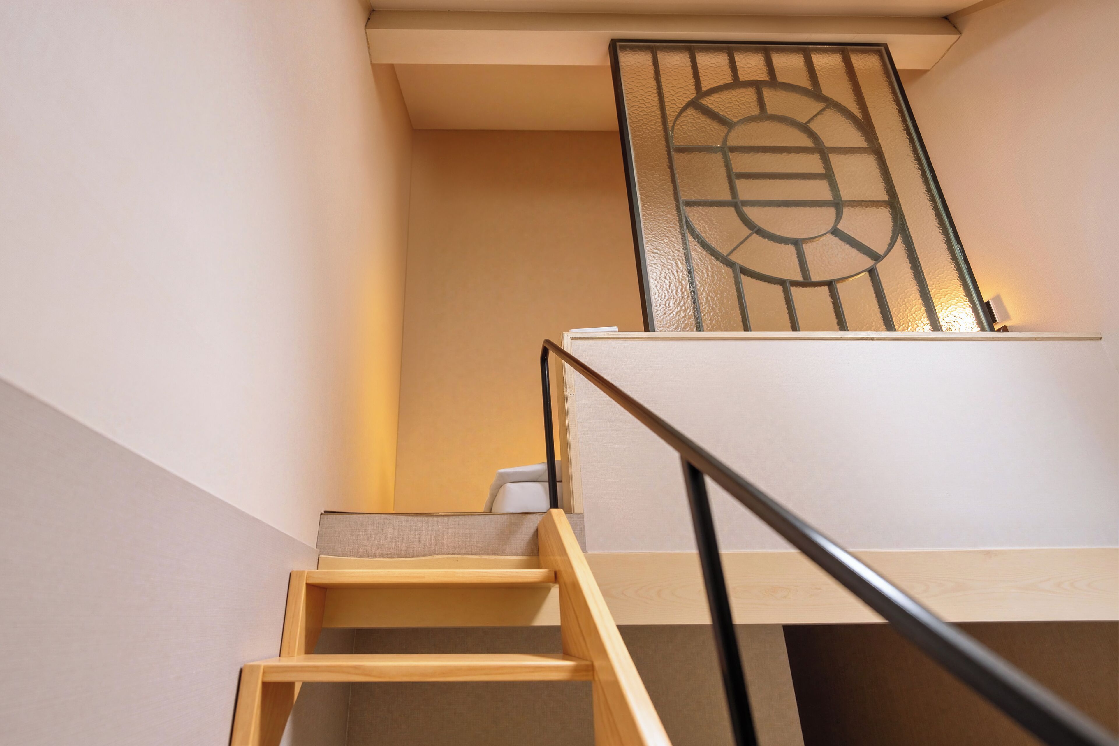 Un escalier en bois, doté d’une rampe métallique, mène à un palier où se trouve une porte en verre.