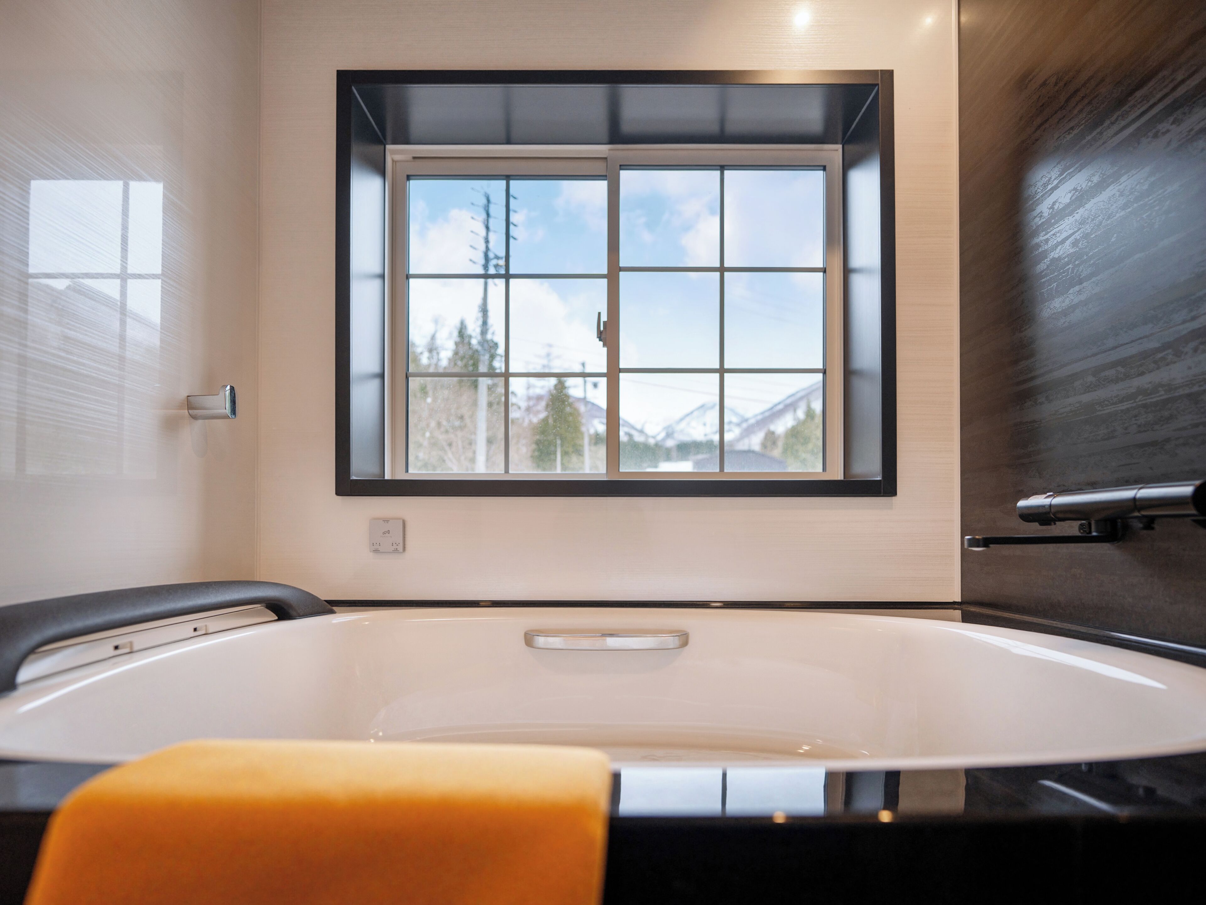A bathroom with a bathtub, a window with a view of mountains, and a wooden wall.