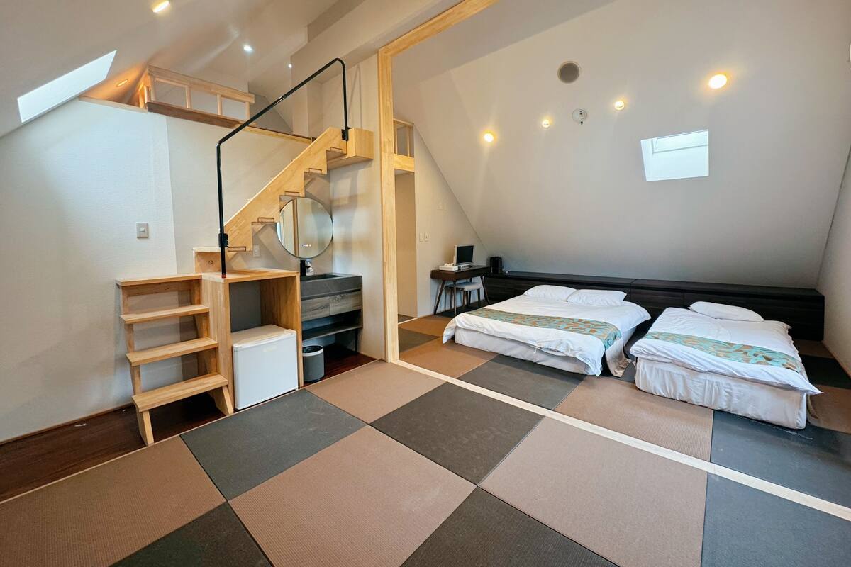 Une chambre avec un lit de style industriel, un bureau avec un ordinateur et un petit coin salon.