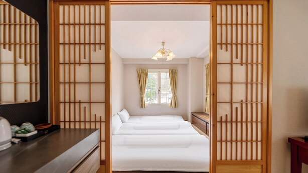 A traditional Japanese-style room with a bed, wooden sliding doors, a dresser, and a mirror.