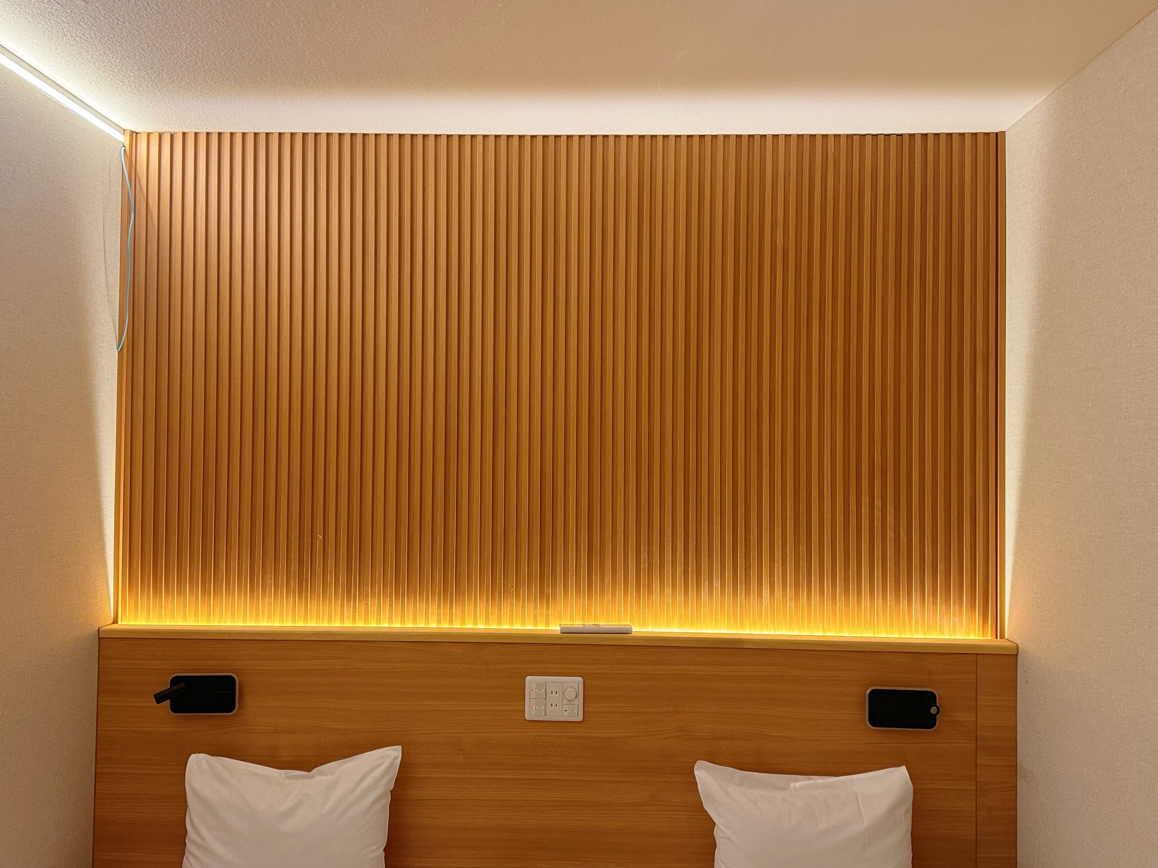 A hotel room with a wooden headboard, two white pillows, and a bedside table with a power outlet.