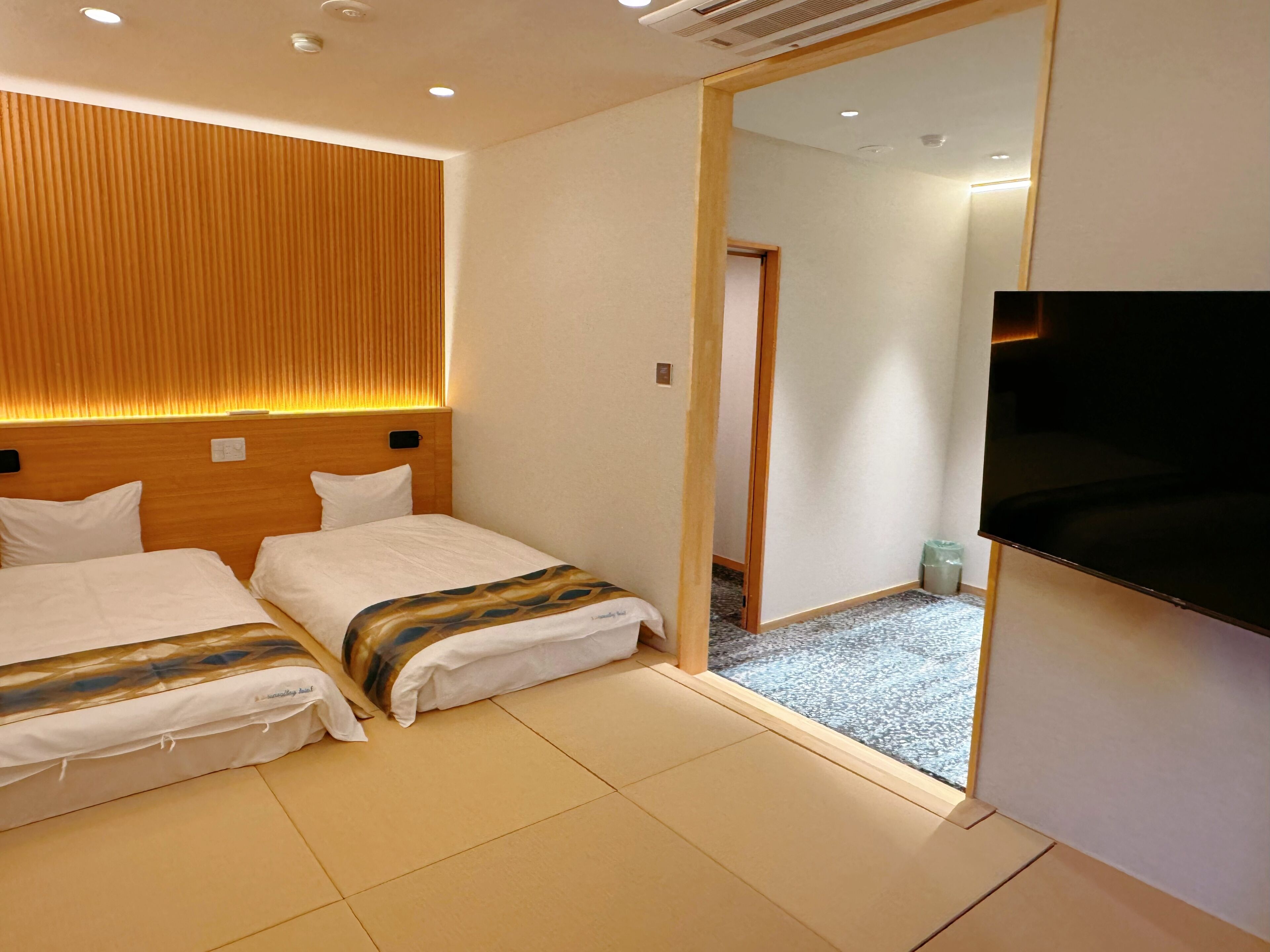 A hotel room with two beds, a wooden headboard, a flat-screen TV, and a small trash bin.