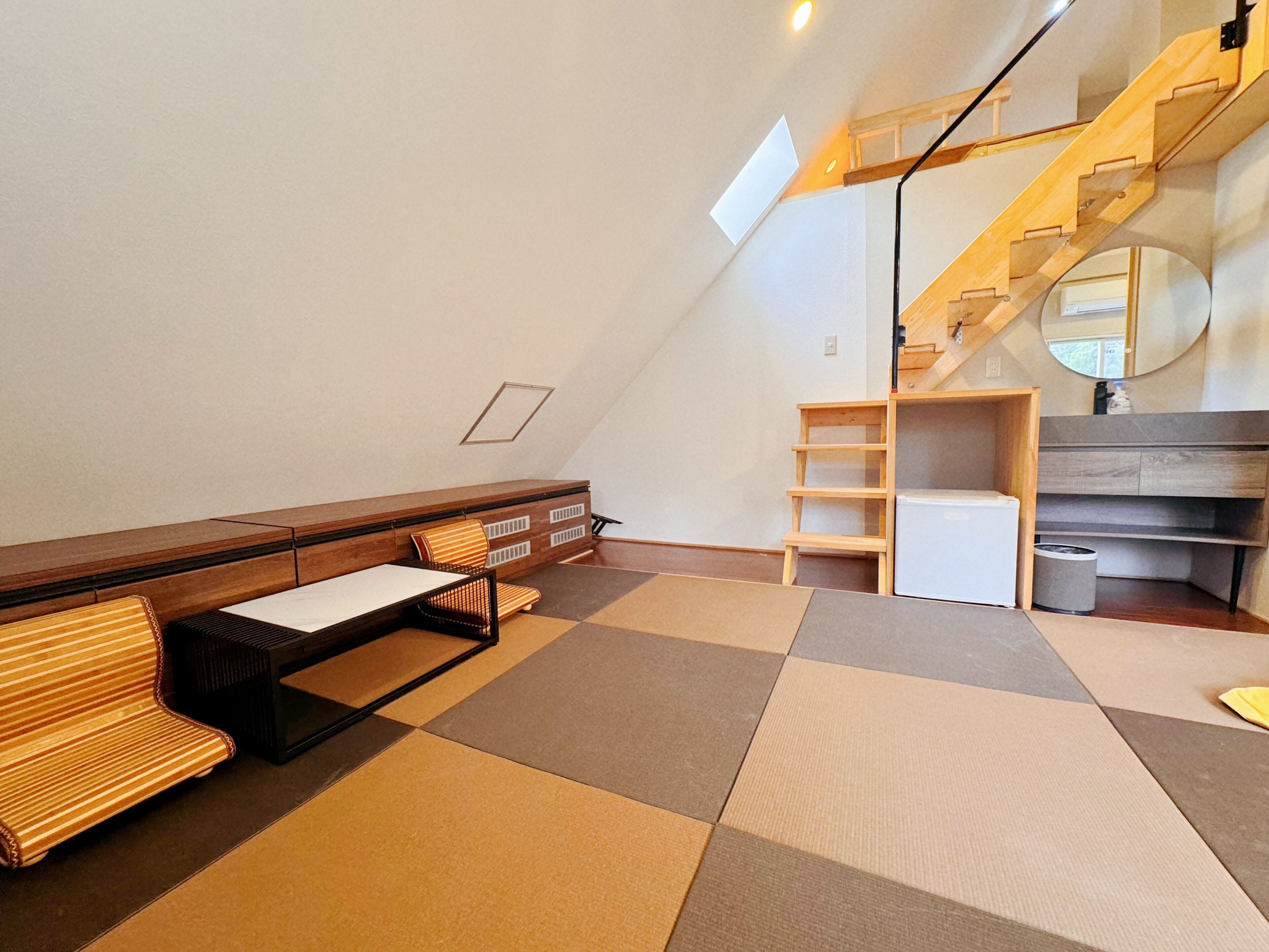 A modern, minimalist room with a sloped ceiling, a wooden bench, a small table, a ladder, and a mirror.