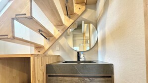 A bathroom with a wooden vanity, a round mirror, and a bottle of hand soap.