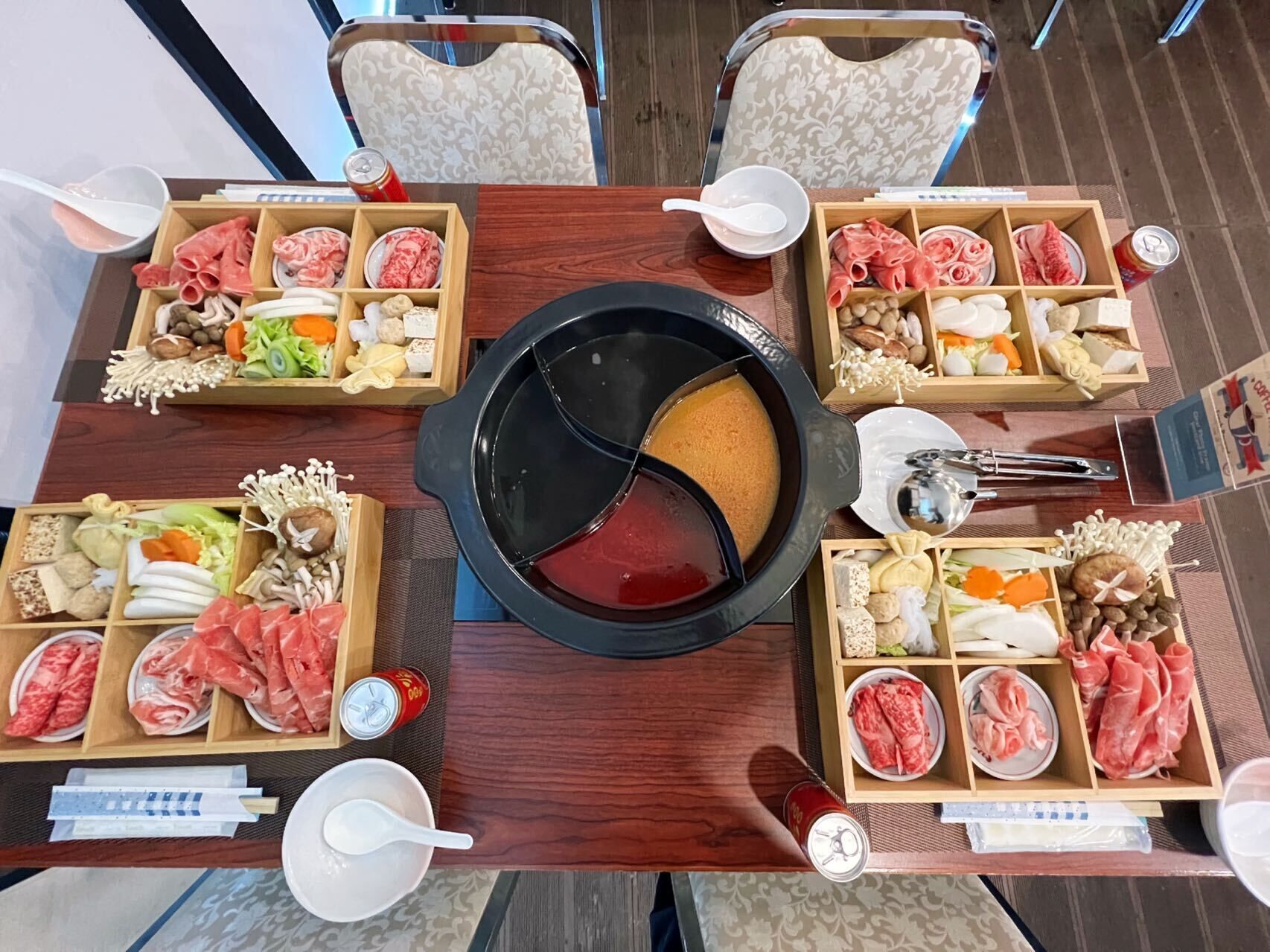 Una mesa de comedor con múltiples bandejas de comida de madera, una olla caliente en el centro y dos sillas.