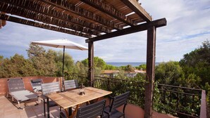 An outdoor patio with a wooden table and chairs, a pergola, and a view of the sea.