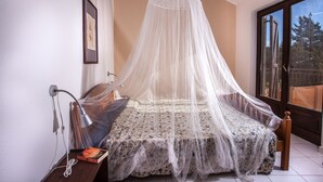 A bedroom with a canopy bed, a bedside table with a lamp, and a window with a view of trees.