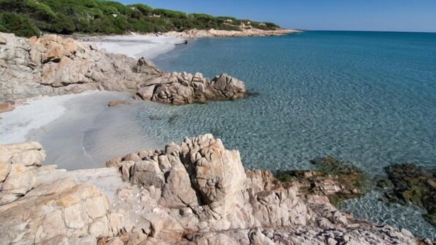 A rocky coastline with clear blue water and a sandy beach.