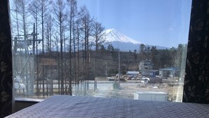 A bed with a quilted white cover, a window with a view of a snow-capped mountain, bare trees, and a parking lot with vehicles. - Asia Hotel Kawaguchiko (Fujikawaguchiko)