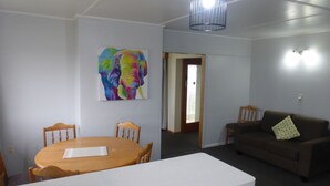 A room with a dining table, chairs, a sofa, and a colorful elephant painting on the wall.