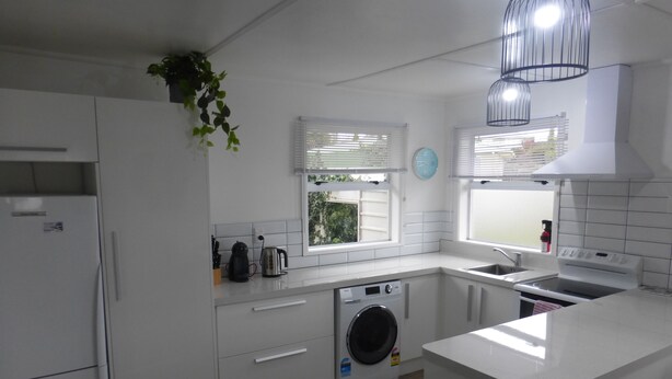 A modern kitchen with white cabinetry, a built-in washing machine, a stove, and a sink.