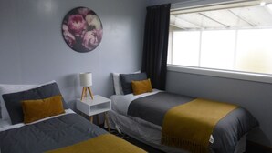 A hotel room with two beds, a nightstand, a lamp, a painting, and a window with curtains.