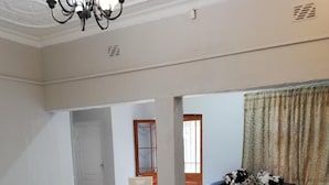 Un coin repas avec une table ronde et des chaises, un lustre, et une vue sur le salon à travers une porte ouverte.