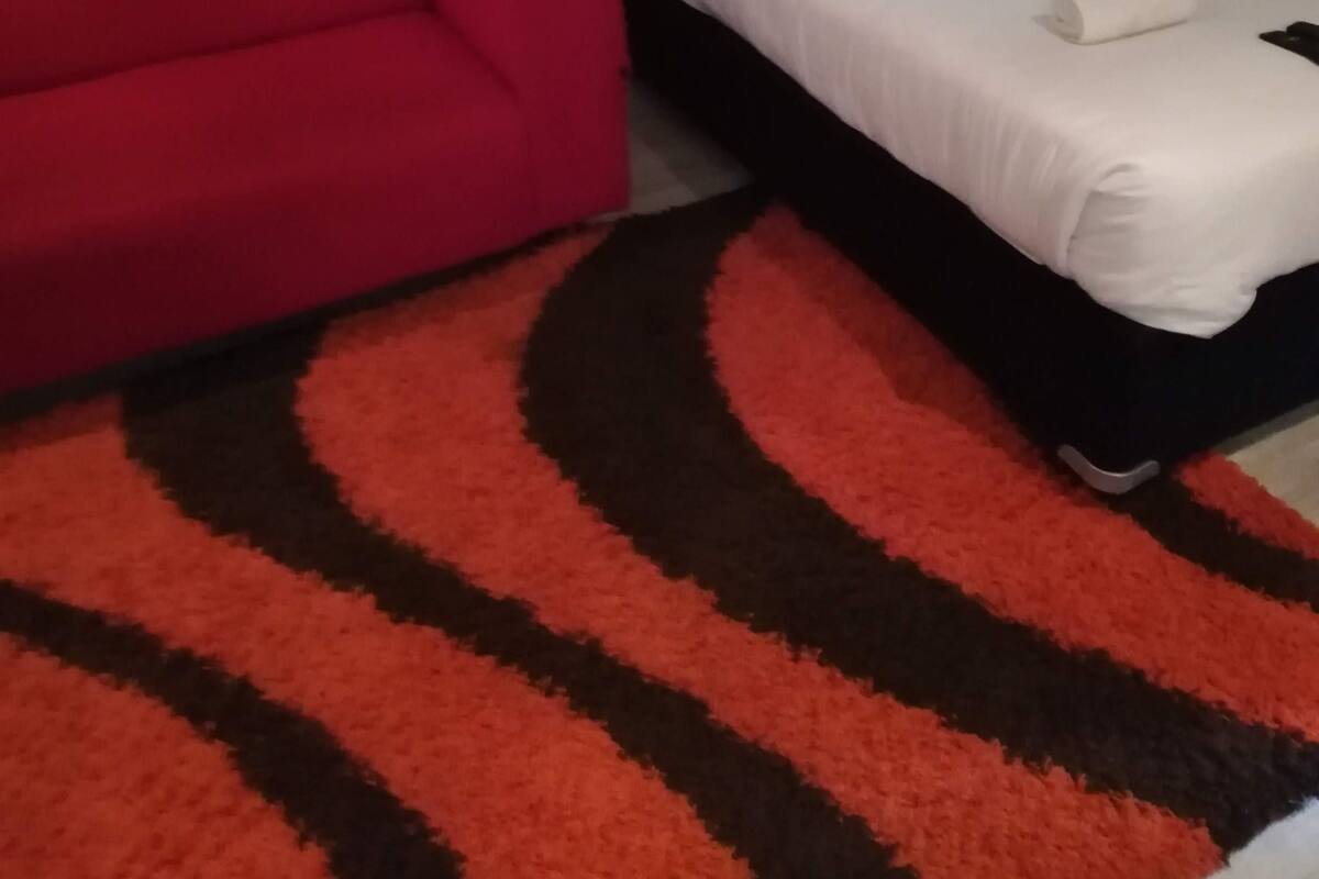 Une petite pièce avec un canapé rouge et un lit simple recouvert de linge de lit blanc.