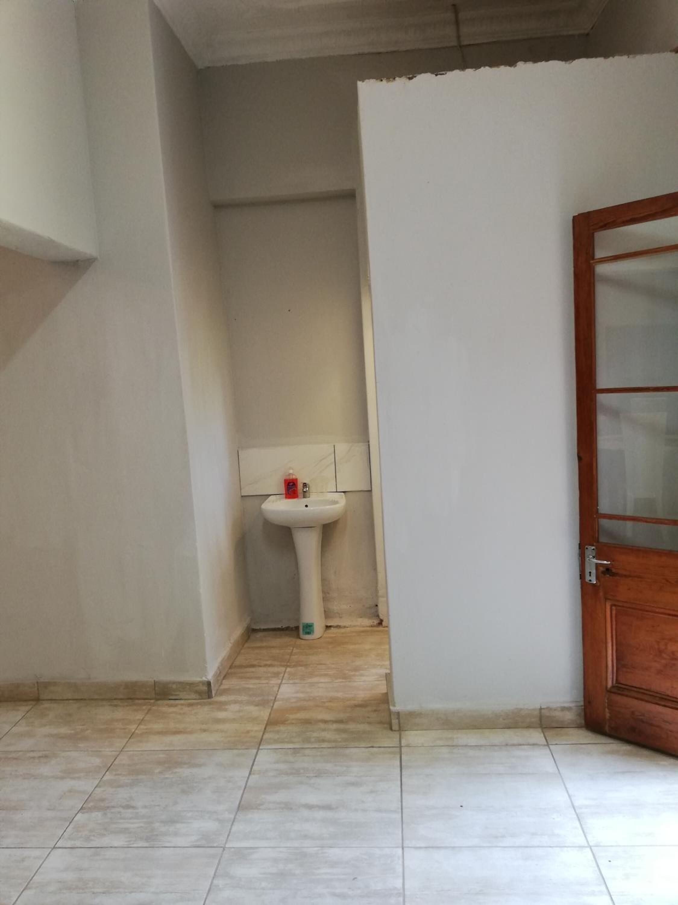 A room with a tiled floor, a white sink with a soap dispenser, and a wooden door with glass panels.