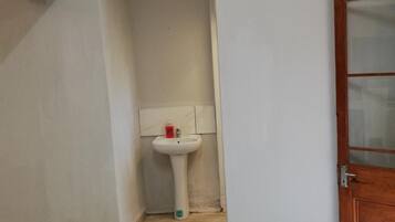 A room with a tiled floor, a white sink with a soap dispenser, and a wooden door with glass panels.