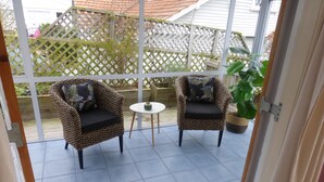 Een overdekt terras met twee rieten stoelen en een kleine tafel.