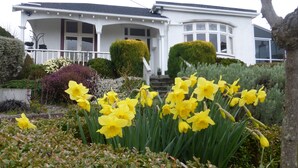 Een wit huis met een veranda en een tuin vol gele bloemen.