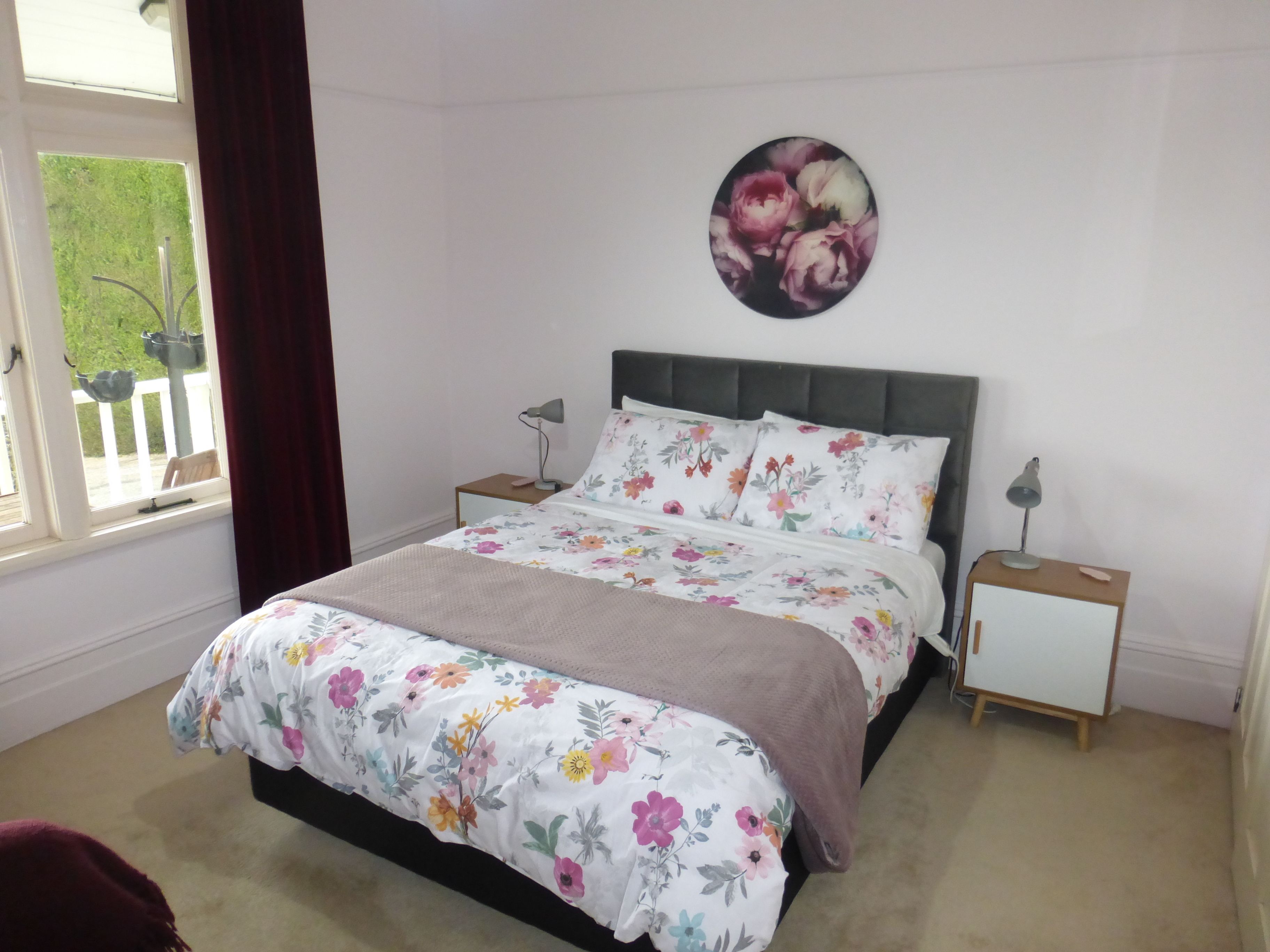 A bedroom with a bed, two bedside tables, a window with curtains, and a wall-mounted picture.