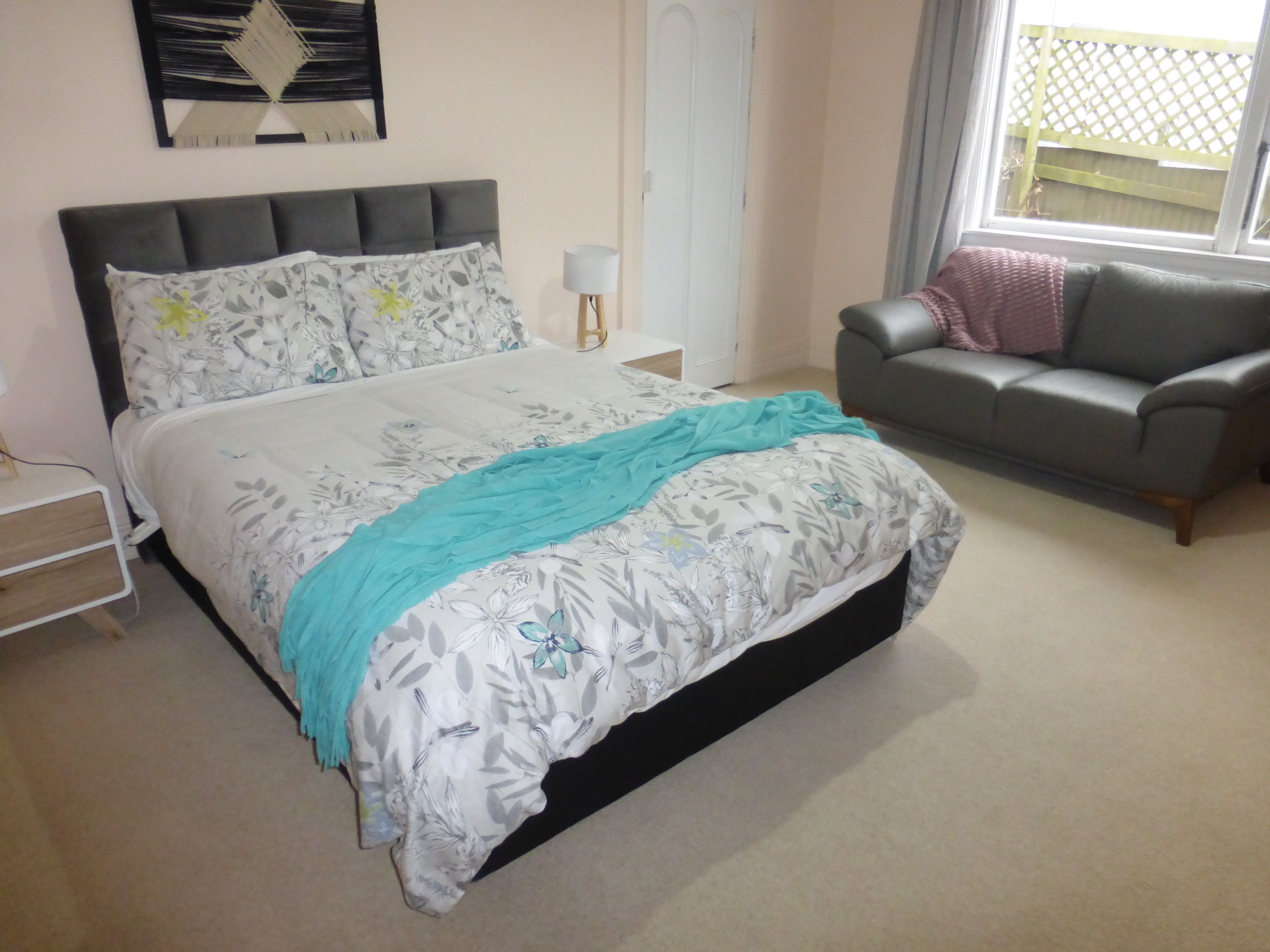 A bedroom with a bed, a grey sofa, a window, and a door.