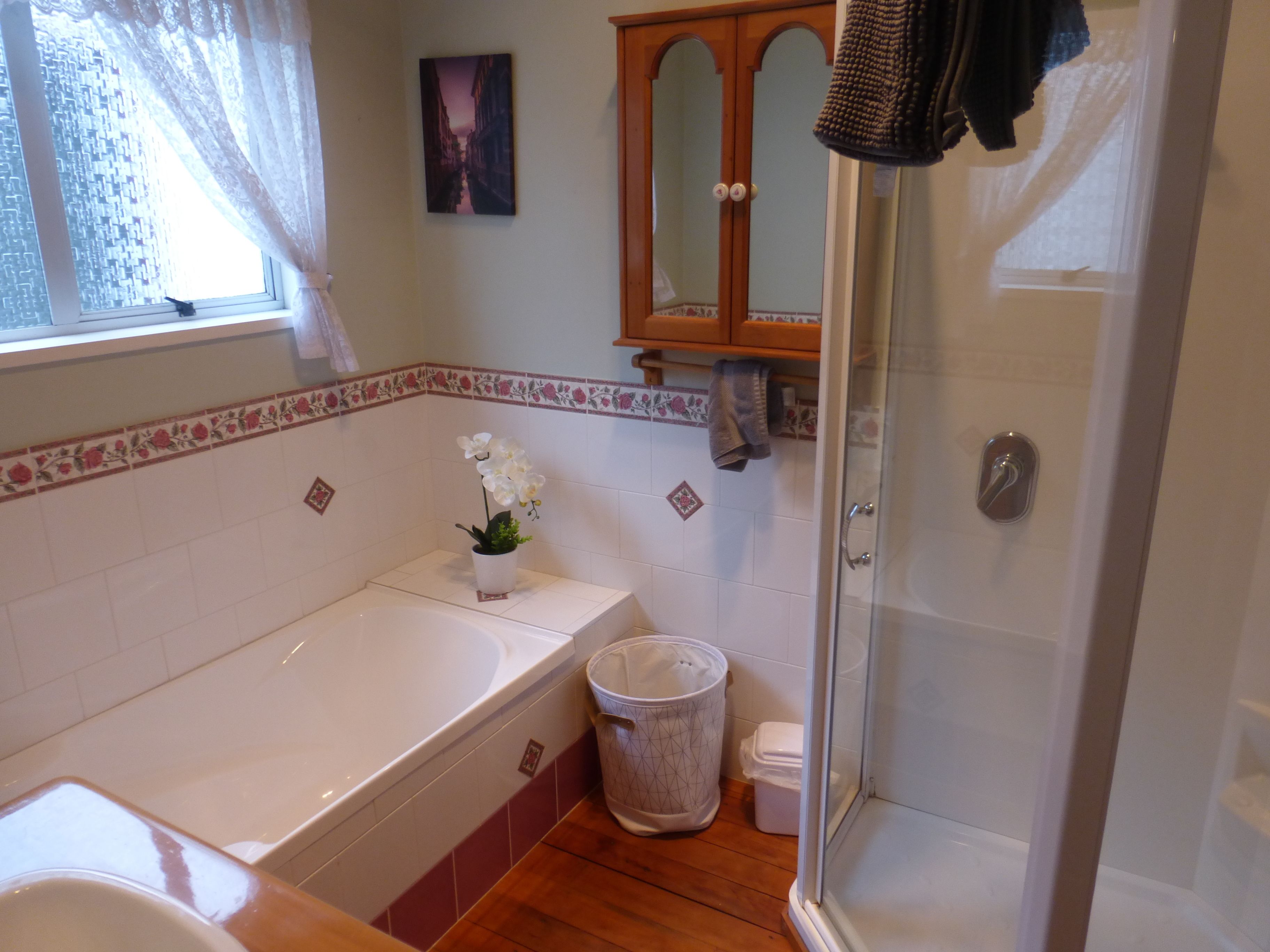 A bathroom with a bathtub, a glass shower enclosure, a waste basket, and a towel rack.