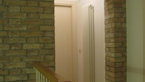 A staircase with a wooden handrail leading to a room with a brick wall and a white radiator. - Al Piccolo Clarin (Mestre)