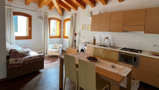 A spacious kitchen with wooden beams, a dining area with a table and chairs, and a cozy seating area with a sofa. - Al Piccolo Clarin (Mestre)